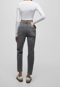 Jeans grigi ad alta vita con gamba dritta e tasche posteriori, abbinati a un crop top bianco a maniche lunghe e sneakers chiare.