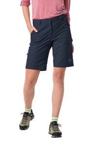 Námořnické modré venkovní kraťasy s volným střihem, zipovými kapsami a odolnou tkaninou. V kombinaci se šedými turistickými botami a ponožkami s zelenými akcenty.