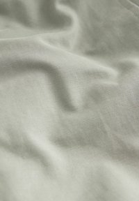 Tessuto verde chiaro con una superficie liscia e leggermente texture, contraddistinto da pieghe delicati e un finitura morbida e opaca.