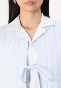 Jasnoniebieski, fakturowany top z pionowymi paskami oraz zawiązywaniem z przodu. Posiada białą, kołnierzykową wewnętrzną koszulę z zapięciem na guziki.