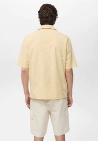 Korte mouwen gele shirt met een textuurpatroon, kraag en een relaxed fit, gecombineerd met lichtbeige cargoshorts met zakken.