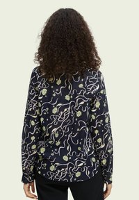 Marinebluse med et flydende, abstrakt design med grønne og cremefarvede former. Lange ærmer og knaplukninger ved håndleddene fuldender udseendet.