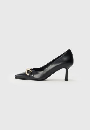 Sandal com salto preto em couro, apresentando um bico fino e um salto de 7 cm. Acento notável com hardware dourado em forma de coração de um lado. Textura suave no geral.