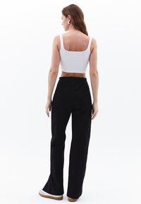 Vit kort crop-top och svarta vida byxor med hög midja, sidofickor och en texturerad tyg. Skorna är vita med en tan-färgad sula.