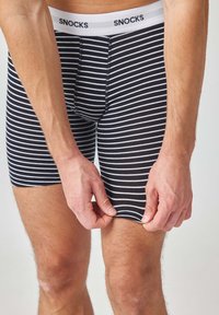 Boxer briefs a righe bianche e nere con un elastico bianco in vita su cui è presente il marchio "SNOCKS". Tessuto morbido e aderente con una texture liscia.