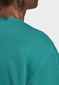 Turkos crewneck-tröja med texturerad yta. Har synliga sömmar längs axeln och en avslappnad passform vid halslinningen.