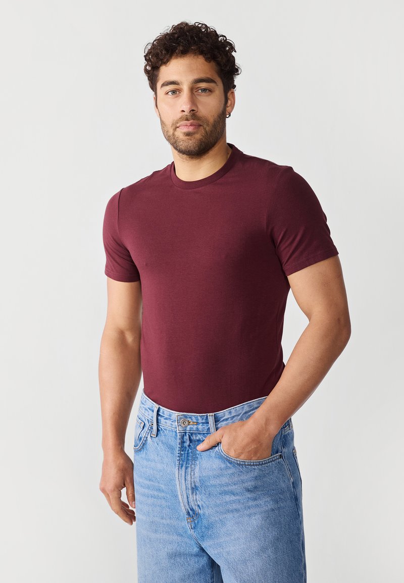 Bordeaux korte mouw t-shirt gemaakt van zacht katoen, gecombineerd met lichtblauwe high-waisted jeans. Eenvoudige ronde halslijn en aansluitende pasvorm.