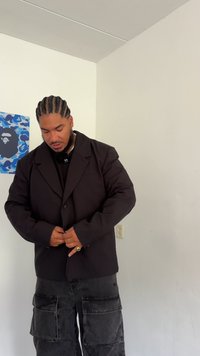 Blazer nero oversize realizzato in tessuto morbido, con chiusura a un bottone. Indossato sopra una maglietta scura e pantaloni cargo, all'interno.
