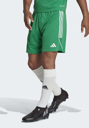 Groene sportshorts met witte strepen, gecombineerd met zwarte voetbalschoenen met blauwe accenten en witte crew-sokken.