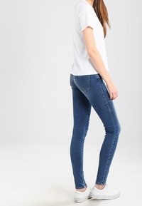 Vit kortärmad topp tillsammans med åtsittande blå jeans och vita sneakers. Jeansen har en klassisk femficksdesign och en lätt blekning.