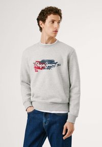 Sudadera gris de algodón con puños y dobladillo acanalados, con una impresión gráfica multicolor de "Pepe Jeans London" en el frente. Combinada con jeans azules.
