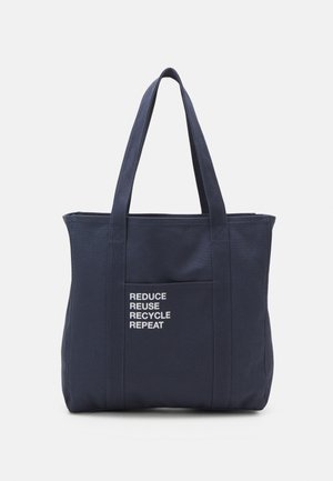 Tmavě modrá plátěná taška s dvěma uchy a přední kapsou, s bílým nápisem "REDUCE REUSE RECYCLE REPEAT." Jednoduchý design.