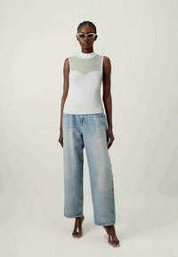 Balta rankovių viršutinė dalis su prikimštu dizainu, derinama su šviesiai mėlynomis plačiomis kelnėmis; modelis nešioja skaidrias rėmo akinius ir permatomus sandalus.