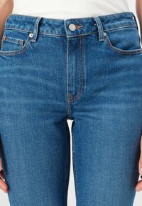 High-waisted blue denim jeans with orange stitching, five pockets, and a metal button closure, featuring a straight-leg fit and smooth texture.