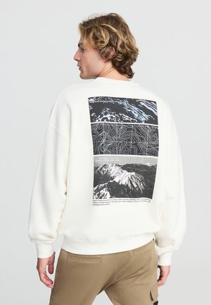 Felpa bianca con una grafica in bianco e nero sul retro, che presenta la topografia di una montagna e fotografie. Vestibilità rilassata con polsini a costine.
