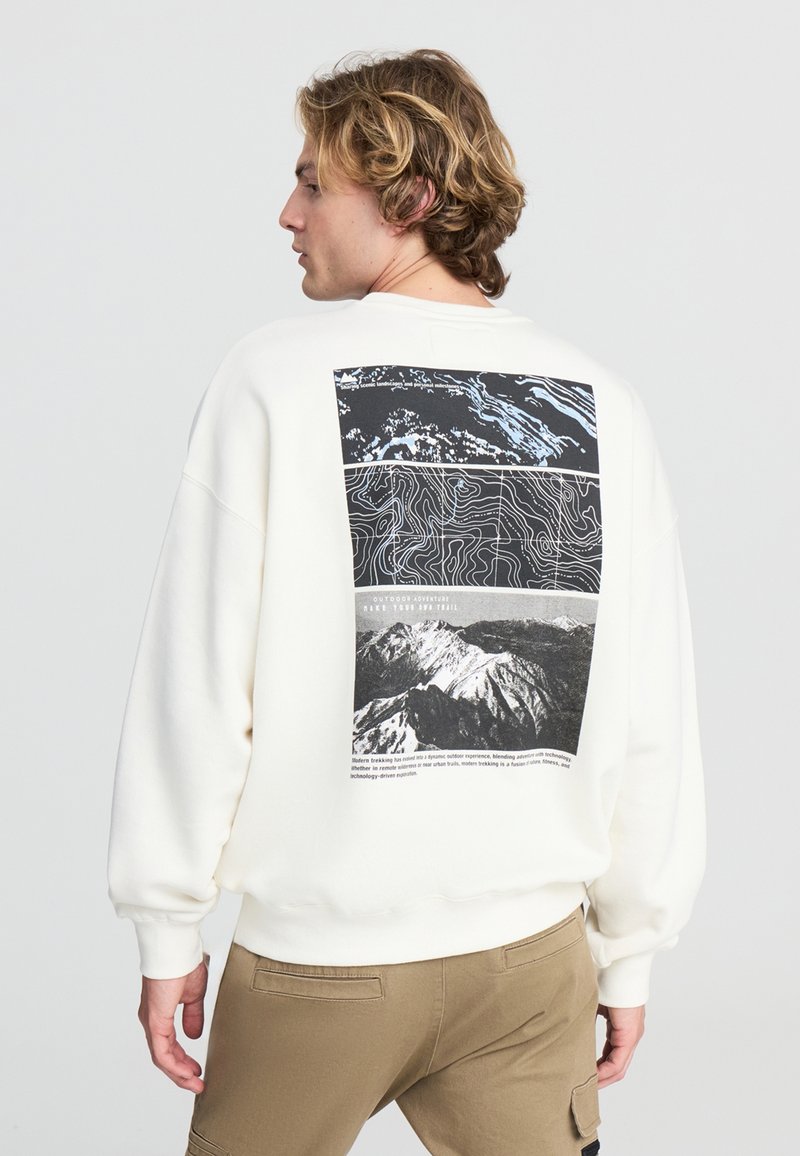 Felpa bianca con una grafica in bianco e nero sul retro, che presenta la topografia di una montagna e fotografie. Vestibilità rilassata con polsini a costine.
