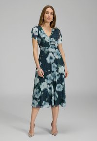 Robe florale en marine et bleu sarcelle avec un décolleté en V, des manches courtes bouffantes et une jupe fluide arrivant au genou. Elle présente un corsage froncé et un tissu léger.