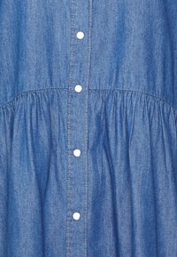 Abito di jeans in una tonalità azzurro chiaro, con abbottonatura, vita arricciata e texture morbida. La cucitura bianca in evidenza aggiunge un tocco di dettaglio.