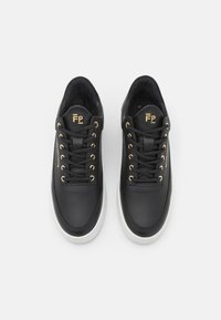 Černé kožené tenisky se zlatými očky a logem, bílé podrážky, zaoblený tvar a polstrovaný límec. Hladký povrch s minimem designových detailů.