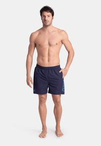 Pantaloni da bagno navy con cintura elastica, dotati di un motivo grafico blu chiaro sul lato. Realizzati in tessuto leggero e ad asciugatura rapida.