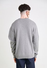 Gray knitted sweater with a round neckline and ribbed trims, featuring a loose fit and soft texture, viewed from the back.
