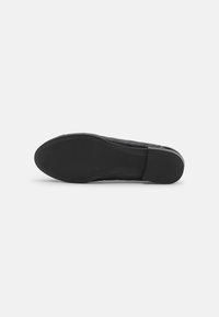 Suela de zapatilla negra con una superficie de goma texturizada y un sutil patrón ondulado. Presenta una puntera redondeada y una ligera elevación en el talón.