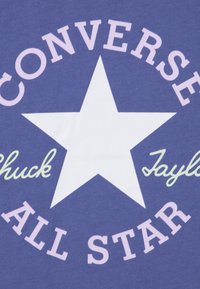Μωβ ύφασμα με ένα λευκό αστέρι στο κέντρο, με την επιγραφή "CONVERSE" πάνω και "ALL STAR" κάτω, και το όνομα "Chuck Taylor" σε ανοιχτό πράσινο.