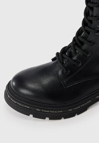 Bottines noires en cuir lisse avec un bout rond, dotées de lacets, d'œillets métalliques et d'une semelle texturée portant la marque "TOM TAILOR".