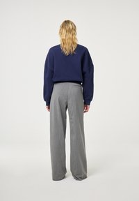 Felpa oversized blu marina abbinata a pantaloni larghi grigio a righe. Il tessuto morbido e la vestibilità rilassata creano un look contemporaneo.