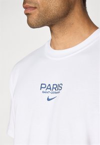 Hvid bomulds t-shirt med blåt broderet tekst "PARIS SAINT-GERMAIN" og "Nike" logo. Rund hals og korte ærmer. Blød tekstur.