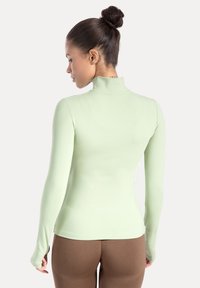 Top de manga larga color verde menta con cuello alto, hecho de material elástico. Cuenta con un pequeño detalle de la palabra 'TRUST' en el escote.