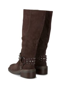 Botas de ante marrón hasta la rodilla con un tacón grueso, que presentan una correa decorativa con tachuelas plateadas y acentos de hardware. Acabado suave y texturizado.