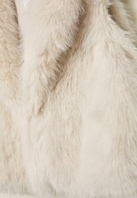 Weicher Kunstpelz in Cremefarbe mit einer strukturierten, flauschigen Oberfläche; zeigt unterschiedliche Längen und Dichten der Fasern für zusätzliche Dimension.