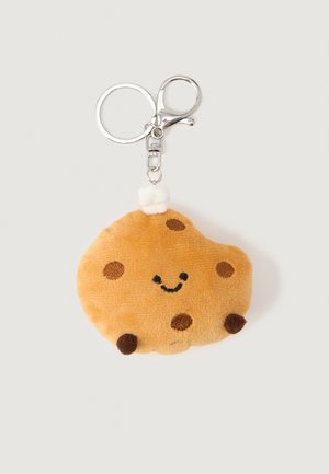 Porte-clés en peluche en forme de biscuit aux pépites de chocolat souriant, avec un petit chapeau de chef blanc attaché à un anneau et un fermoir en métal argenté.