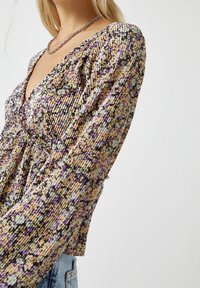 Langärmliges Oberteil mit einem strukturierten Muster in Lila, Beige und Schwarz. V-Ausschnitt-Design mit Raffung in der Taille.