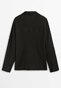 Chemise noire à manches longues en tissu texturé, avec poignets boutonnés et détail d’empiècement au dos, vue de dos sur fond blanc.