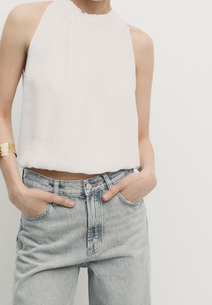 White halter top made of smooth fabric, featuring a gathered neckline. Paired with light blue high-waisted denim jeans with front pockets.