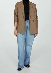 Brown blazer with double buttons, layered over a black turtleneck. Paired with light blue wide-leg jeans and black shoes.