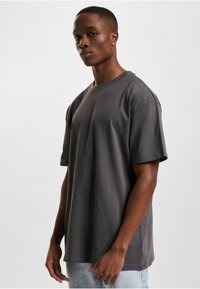 Pernelyg didelis pilkas medvilnės marškinėliai su apvalia kaklo iškirpte, trumpomis rankovėmis ir lygiu paviršiumi. Sujungti su šviesiai mėlynomis džinsinėmis kelnių.