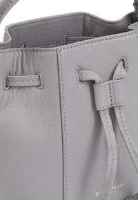 Grijze leren emmer tas met een gestructureerd oppervlak, trekkoordsluiting en zichtbare stikdetails. Merkennaam gebosseld aan de zijkant.