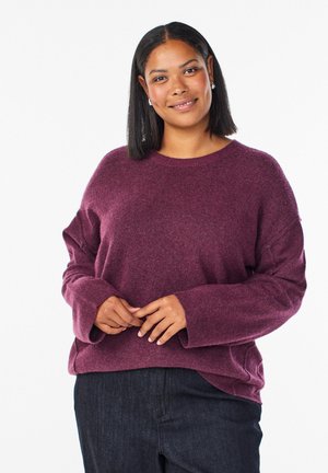Maglione a maglia bordeaux con scollatura rotonda, maniche lunghe e vestibilità rilassata; morbida texture, polsini e orlo a costine. Abbinato a jeans scuri.
