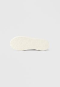 Λευκή σόλα παπουτσιού από καουτσούκ με υφή, που διαθέτει ανάγλυφα λογότυπα και κυκλικά σχέδια για πρόσφυση. Λεπτό, ομαλό φινίρισμα συνολικά.