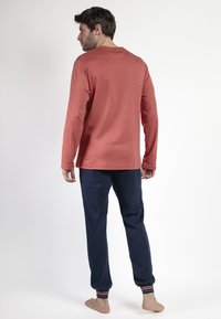 Camisa de manga larga color óxido combinada con pantalones de chándal azul marino con puños a rayas. El conjunto está hecho de una tela suave y ofrece un ajuste cómodo.