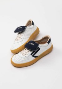 Hvide lædersneakers med en tekstureret marineblå tunge, lyse snørebånd og gummisål. Har et marineblåt accentbånd langs siderne.