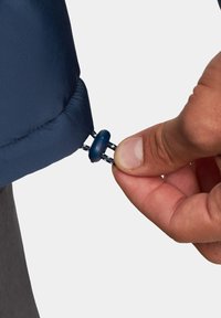 Navy izolowana kurtka z mankietami i systemem ściągającym; ręka trzyma niebieski suwak przymocowany do pętli do zaciągania.