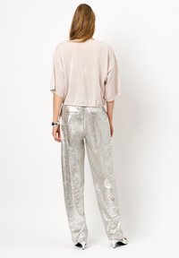 Lichtbeige oversized top met korte mouwen, gecombineerd met glanzende zilveren, losse broek met achterzakken. Soepele textuur en glanzende afwerking.