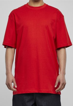 Person wearing a plain bright red oversized short-sleeve T-shirt and dark pants, shown from shoulders to mid-thigh against gray background.