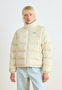 Beige puffer jacket with a high collar, zip closure, and horizontal stitching; features a gray logo on the chest and elastic cuffs.