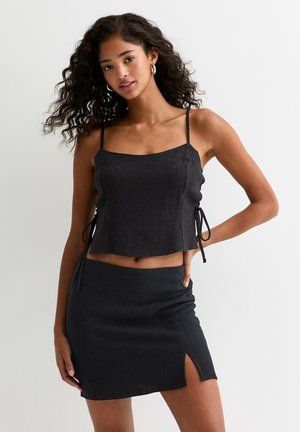 Top corto de mezclilla negra con detalles de lazo a los lados, combinado con una mini falda a juego que cuenta con una abertura lateral. Textura suave, diseño casual.