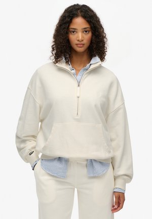 Crème-kleurige sweatshirt met een kwart-rits, relaxed fit en een voorzak. Gelaagd over een blauw-wit gestreept overhemd met kraag.